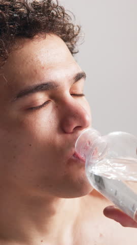 Fitness, tired and man drink water in studio for wellness, workout recovery and health. Bottle, thirsty athlete and hydration for exercise break, breathing or refreshing liquid on white background