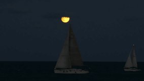 Peaceful summer night scene with two sailboats sailing across the sea under a bright full moon partially covered by a drifting cloud - Powered by Shutterstock - Get 15% off with code: PIKWIZARD15