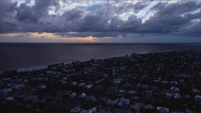 Dark rooftops line a quiet seaside town as a bruised sky thickens, a thin band of sunset glows over calm water, hinting at oncoming weather and restful hush. - Powered by Shutterstock - Get 15% off with code: PIKWIZARD15