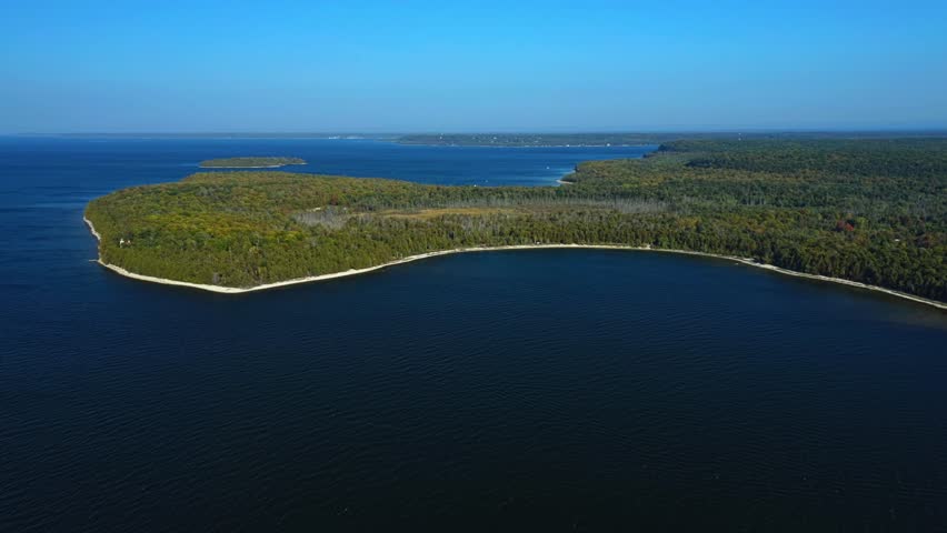 The smooth curve of Door County’s forested shoreline arcs into the bay, where dark blue waters glisten beneath clear skies, tracing the quiet meeting of land and lake.