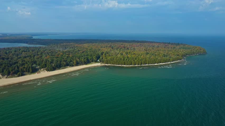 The emerald waters of Lake Michigan curve around a golden shoreline and dense autumn forest, forming the tranquil coastal landscape of Whitefish Dunes State Park in Door County.