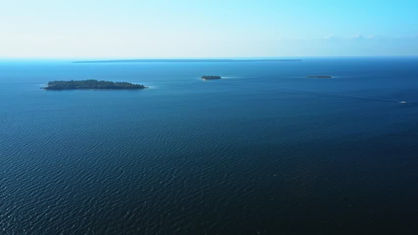 Tiny islands drift within the endless blue of Lake Michigan, their green canopies punctuating the calm expanse of water that stretches toward the hazy horizon of Door County.