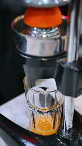 Fresh orange juice being pressed in a glass. Close-up of a metal juicer squeezing fresh orange juice into a transparent glass.