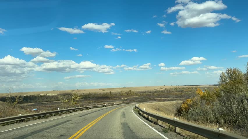 Driving Down a Rural Highway Under Blue Sky and Clouds in Open Prairie Landscape