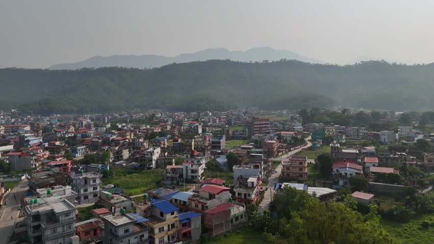 Drone view of Tansen town in Palpa District showing colorful houses, winding streets, and lush surrounding hills under a hazy sky, highlighting charm of a peaceful hill settlement.