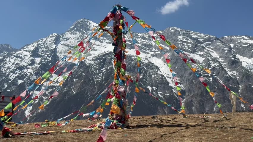 Colorful prayer flags tied to a tall pole near Muktinath in Mustang, Nepal, with snow-covered Himalayan peaks in the background symbolizing peace, spirituality, and mountain devotion.