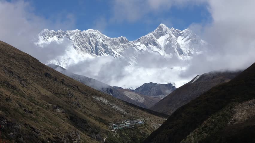 Beautiful view of snow-covered Annapurna peaks seen from Annapurna Base Camp in Kaski District, Nepal, with clouds drifting over rugged hills and a serene Himalayan valley below.