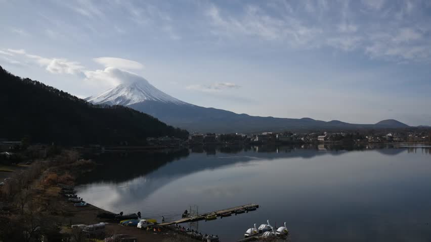 Beautiful view of Mount Fuji reflecting on calm surface of Kawaguchiko Lake under clear blue sky surrounded by trees and soft clouds creating peaceful and scenic landscape Outdoors