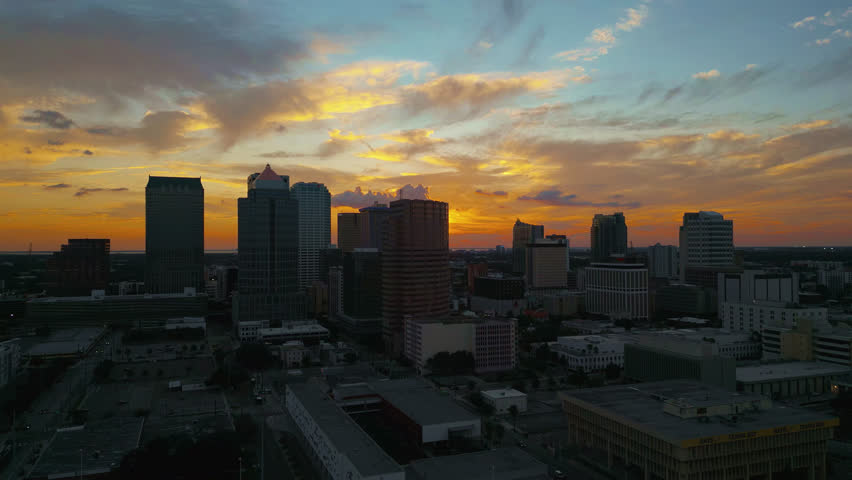 Tampa skyline at sunset with glowing yellow sky and silhouetted buildings, aerial tracking to the right.