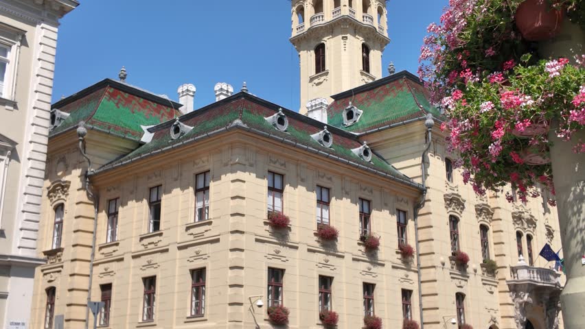 Hungary’s Szeged City Hall exterior shot featuring a vibrant green roof with foreground flowers and a waving flag.
