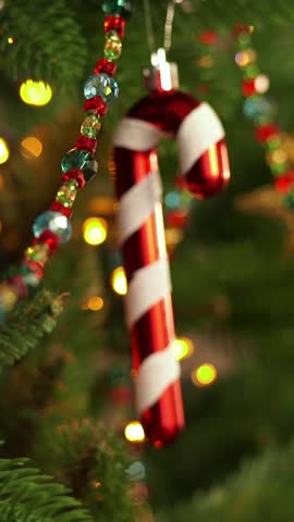 Camera movement on christmas decoration cane on branch of Christmas tree on background of shining garland lights. New Year holiday. Vertical shot