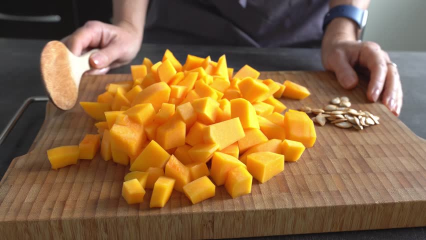 A pumpkin is diced. A woman demonstrates how to cut it. Concept: a cooking vlog.