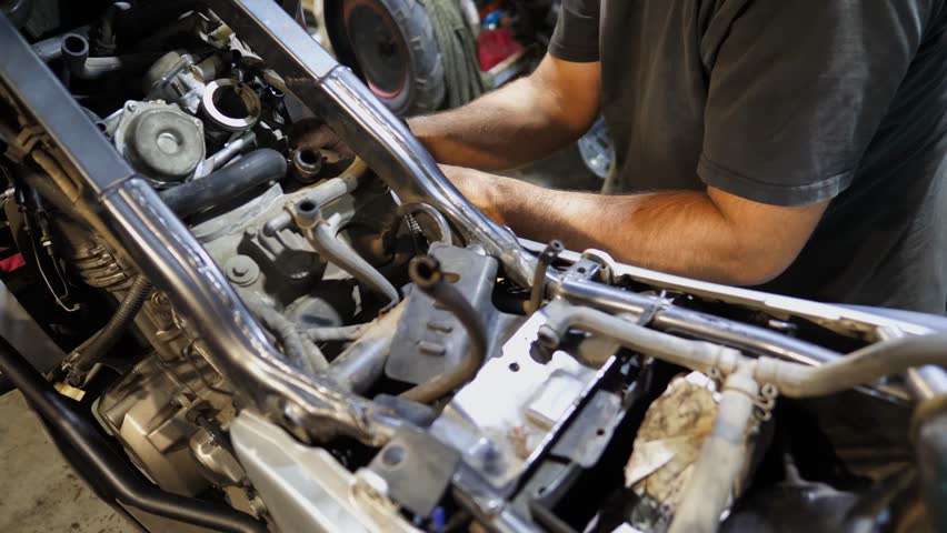 Professional mechanic repairing engine of motorcycle at workshop. Male repairer fixing motor of motorbike using tool at workplace. Adult repairman working at garage. Concept of maintenance service - Powered by Shutterstock - Get 15% off with code: PIKWIZARD15