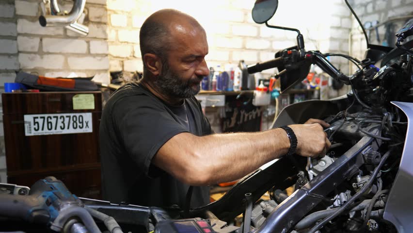 Professional mechanic repairing detail of motorcycle at workplace. Male repairer fixing engine of moto at workshop. Adult repairman mending vehicle motor at garage. Concept of maintenance service - Powered by Shutterstock - Get 15% off with code: PIKWIZARD15