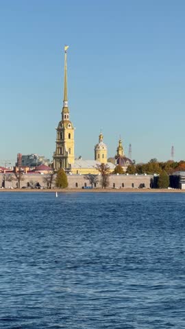 Vertical video of St. Petersburg on sunny autumn day. View from the Neva River of the Peter and Paul Fortress and the spire and domes of the Peter and Paul Cathedral. A beautiful autumn cityscape