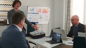 Smiling businessman in jacket opens a suitcase full of dollar bills during office meeting, showing profit and handing money to colleagues with laptops at the table.  - Powered by Shutterstock - Get 15% off with code: PIKWIZARD15