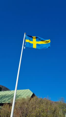 Vertical shot of the Swedish flag fluttering rapidly in strong gusts of wind under a bright blue sky, symbolizing national pride and Scandinavian identity