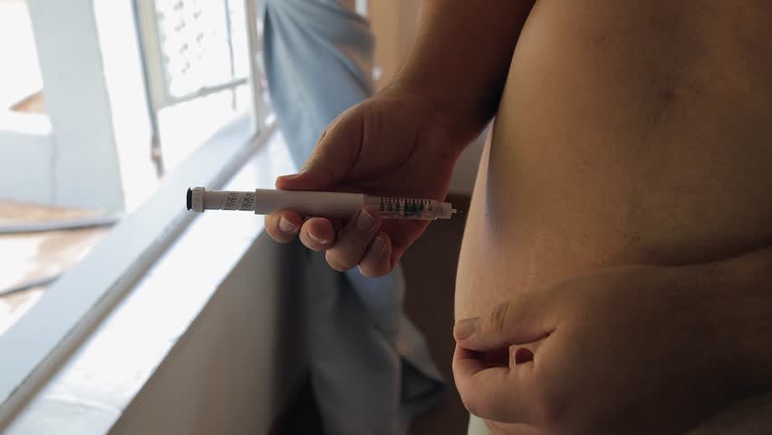 Obese man sticks medication injection pen into subcutaneous belly fat