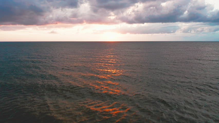 Gentle ripples stretch across the vast ocean as the fading sunlight paints streaks of orange and gold beneath soft clouds drifting through a tranquil horizon.