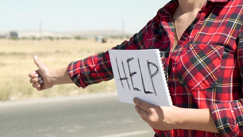 A woman is holding a HELP sign on the side of a road.
