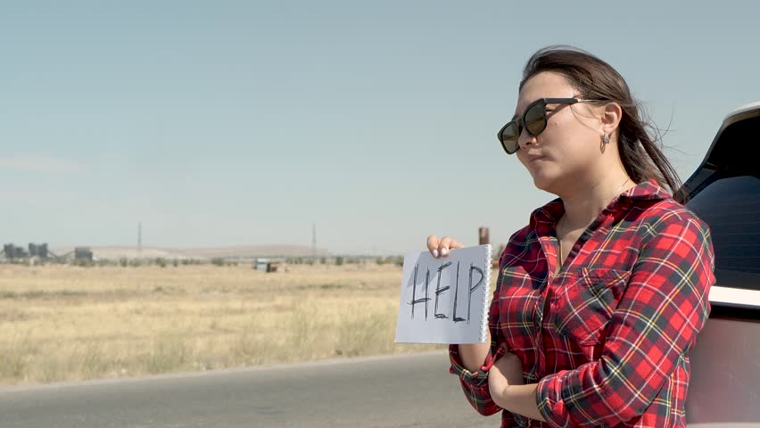 A woman is holding a HELP sign on the side of a road.