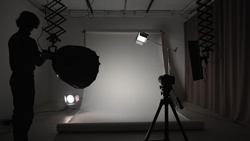 Interior of a professional studio. Professional studio for photo video production filming with modern lighting equipment large white cyclorama background, photographer setting up lights and camera.