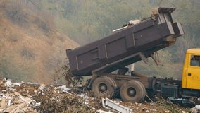 A heavy yellow dump truck unloading a load of garbage and waste at a hillside landfill. Environmental pollution and industrial waste management scene on a gloomy day. Truck dumping trash at a dump. - Powered by Shutterstock - Get 15% off with code: PIKWIZARD15