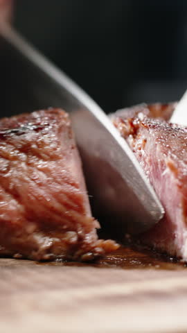 Vertical slow motion video knife cutting grilled beef steak medium well doneness juicy meat close up cinematic lighting gourmet restaurant concept fine dining premium food dark background macro detail