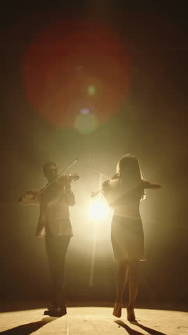 vertical slow motion video of man and woman violinists performing on stage under warm golden light concept of harmony art of sound creative passion and classical music full hd