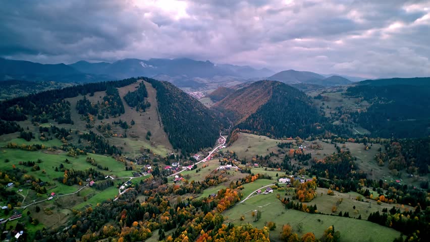 Aerial hyperlapse with lateral orbit motion over autumn mountain valley and forested hills under cloudy sky