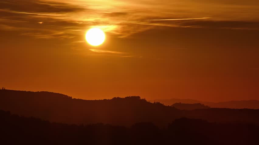 Timelapse of the sun setting over mountain ridge with warm orange sky and fading light at dusk