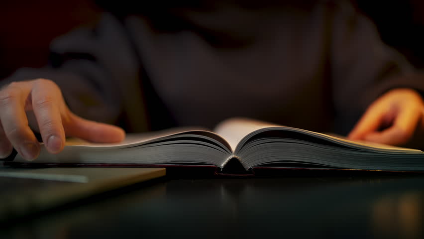 Close-up of woman flipping through pages of large book in city library, hobby