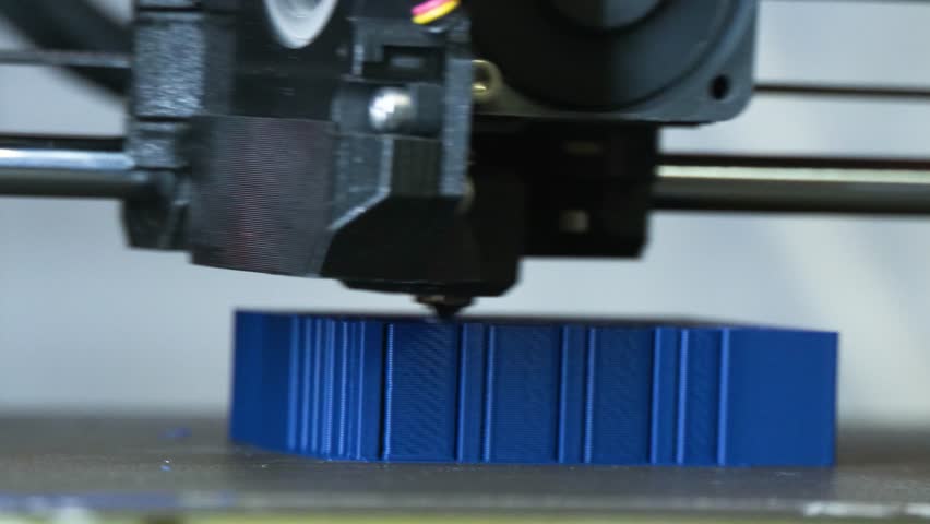 Close-up of 3D printer nozzle creating a blue object. Modern additive manufacturing process in action with melted filament extrusion.