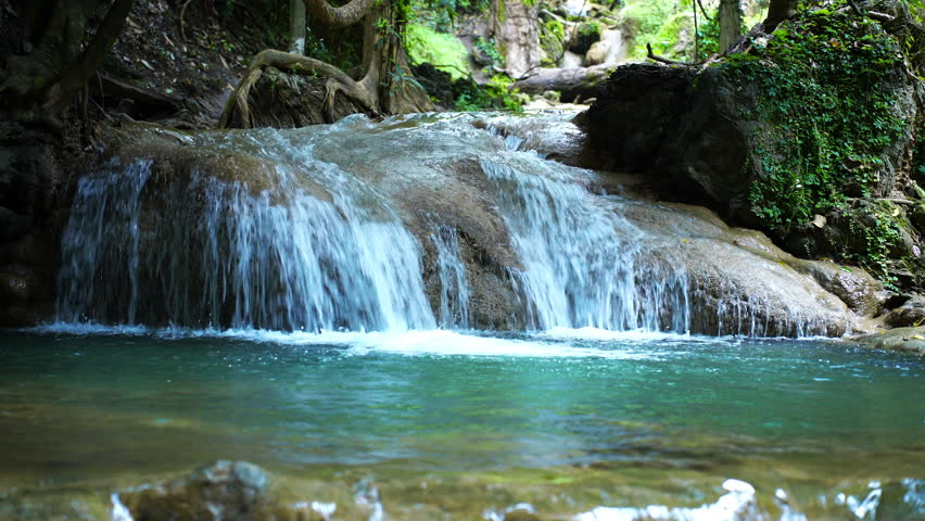 Tropical waterfall cascading over rocky cliff surrounded by lush forest, showcasing raw nature and untouched beauty. Ideal for eco-tourism content, documentaries, and travel visuals.