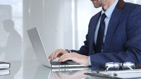 Professional businessman working on laptop computer, typing on keyboard in modern office, managing business tasks. Business people concept - Powered by Shutterstock - Get 15% off with code: PIKWIZARD15