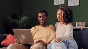 Happy diverse couple sitting on the sofa at home, using a laptop and discussing what they see - Powered by Shutterstock - Get 15% off with code: PIKWIZARD15