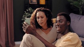 Happy multiracial couple sitting on the floor making a video call on a smartphone at home - Powered by Shutterstock - Get 15% off with code: PIKWIZARD15