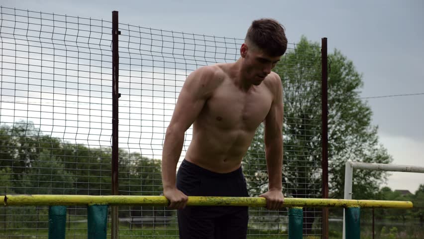 Male shirtless athlete doing push ups on parallel bars at nature. Strong sporty man exercising at sports ground. Young sportsman training hard outdoor. Concept of active sportive lifestyle. Slow mo