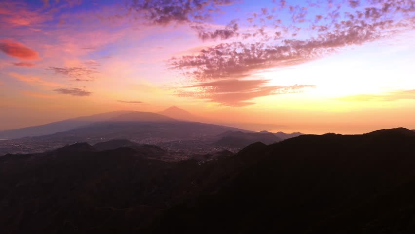 Flight over the dark rocks at sunset time. View on the residential area of Tenerife, the Canary Islands, Spain. Beautiful pink-blue-orange sky at backdrop.