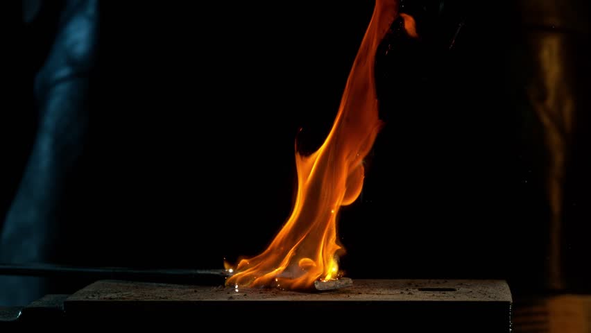 Close-up of blacksmith forging glowing hot iron on anvil with flying sparks. Super slow motion filmed on high-speed cinema camera at 1000 fps