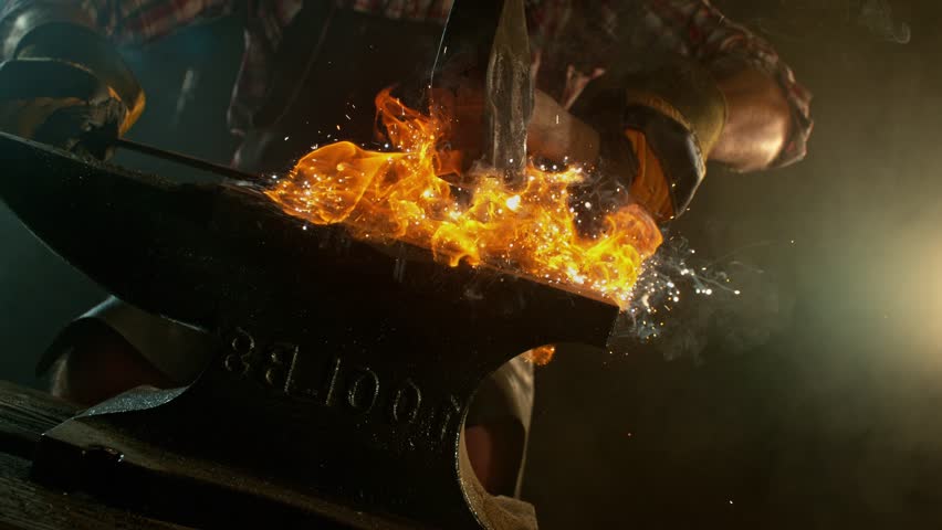 Close-up of blacksmith forging glowing hot iron on anvil with flying sparks. Super slow motion filmed on high-speed cinema camera at 1000 fps
