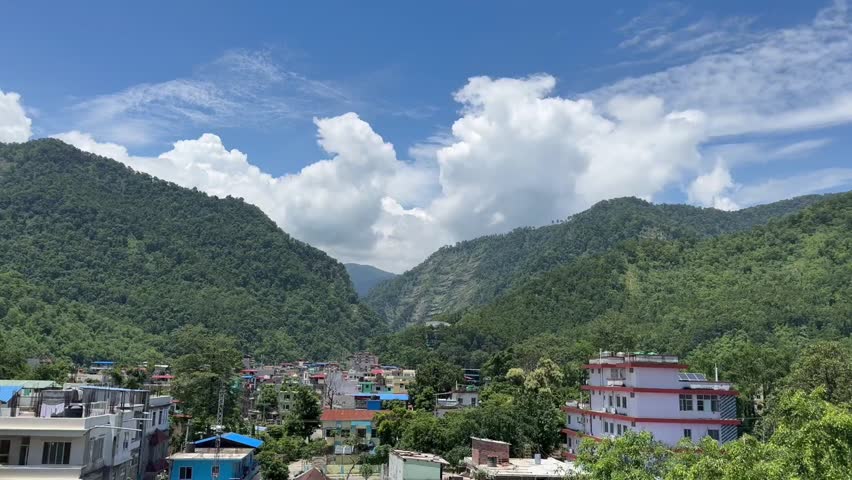Scenic aerial view of Bandipur hill town surrounded by lush green mountains and vibrant houses under bright blue sky with fluffy clouds showing peaceful beauty of Nepal Outdoors