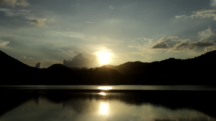 Time-lapse video of colorful clouds rolling over a lake, with a blue mountain range reflection