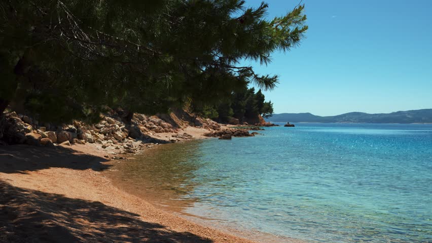 Beautiful Croatia beach with waves, blue sky, and clear seaside water and Mediterranean pine trees.