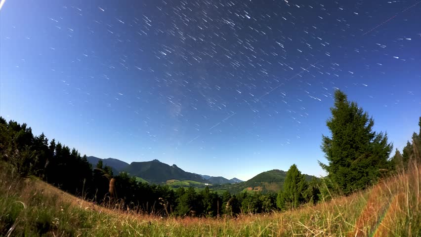 Moonlit night timelapse with star trails over mountain valley