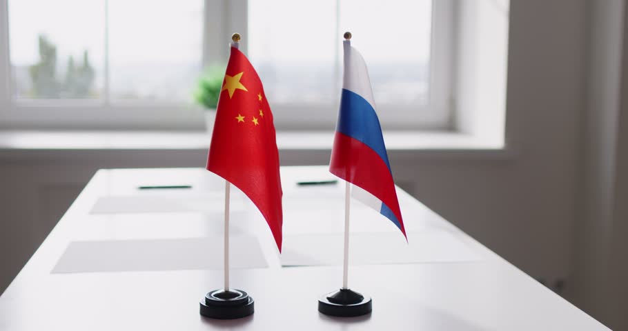 Diplomacy flags signal negotiation and bilateral cooperation. Two miniature national flags face each other on a bright meeting table by a window. Signaling talks. Concept: diplomatic dialogue.