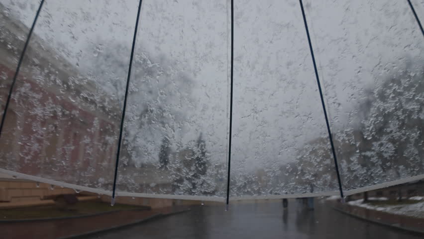 POV video of sleet falls on a transparent umbrella during a walk in the historical center of the European city, young people strolling along empty streets, slow motion