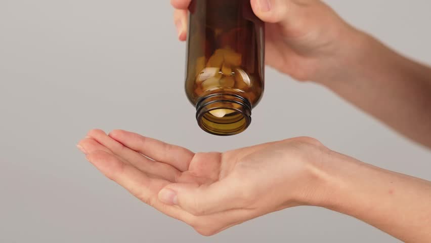 Close-up of a hand full of white tablets being poured from a brown glass bottle. Concept of supplements, multivitamins, pain relief medication and daily healthcare routine.
