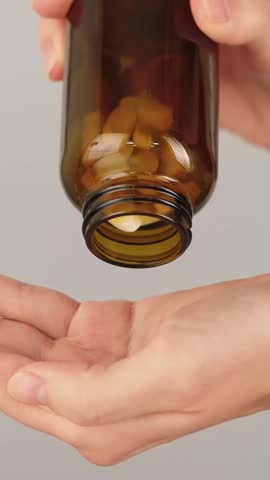 Vertical close-up of a hand full of white tablets being poured from a bottle. Concept of supplements, multivitamins, pain relief medication and daily healthcare routine.