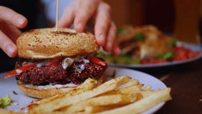 Hands pressing down on a delicious veggie burger with a sesame seed bun served on a plate with crispy french fries in a restaurant, showcasing a healthy and tasty plant based meal option - Powered by Shutterstock - Get 15% off with code: PIKWIZARD15